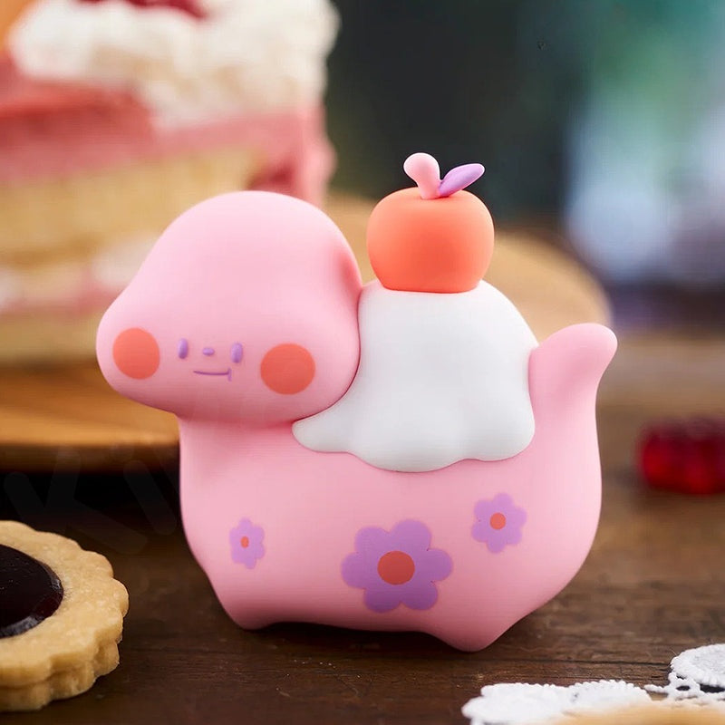Pink cartoon-like figurine with a white cloud and orange flower on a wooden surface.