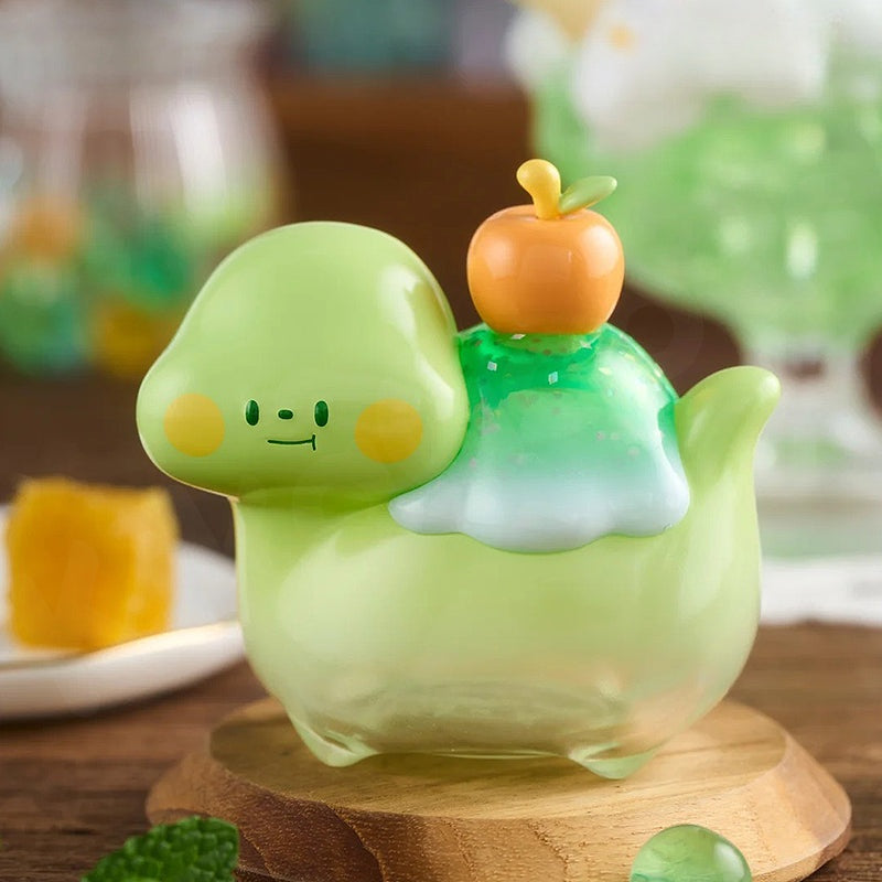 Green cartoon-like creature with a small orange object on its back, sitting on a wooden base.