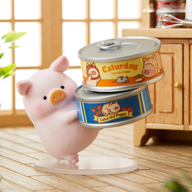 Pink piggy bank with two canned goods labeled 'Saturday' and 'Lulu the Piggy' on a wooden floor.
