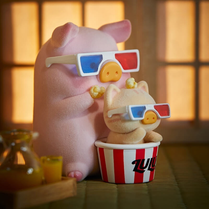 Pink piggy bank and small bear figurine with 3D glasses and popcorn, sitting on a wooden surface.