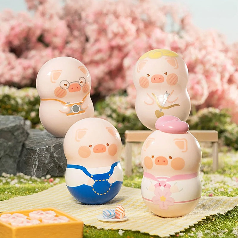 Four pig-shaped toys on a picnic blanket with cherry blossoms in the background