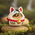 Decorative cat figurine with a traditional outfit on a stone in a natural setting