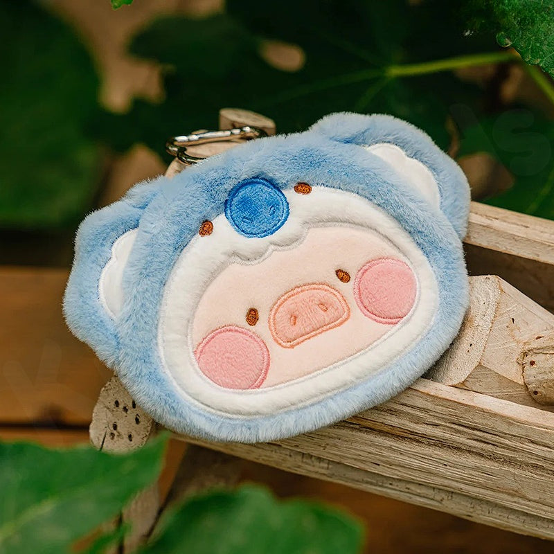 Plush keychain shaped like a blue bear with pink cheeks on a wooden surface.