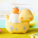 Yellow cartoon-like character with an apple on its head, sitting on a grassy surface with a colorful background.