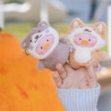 Two small plush toys held in a hand with a blurred outdoor background