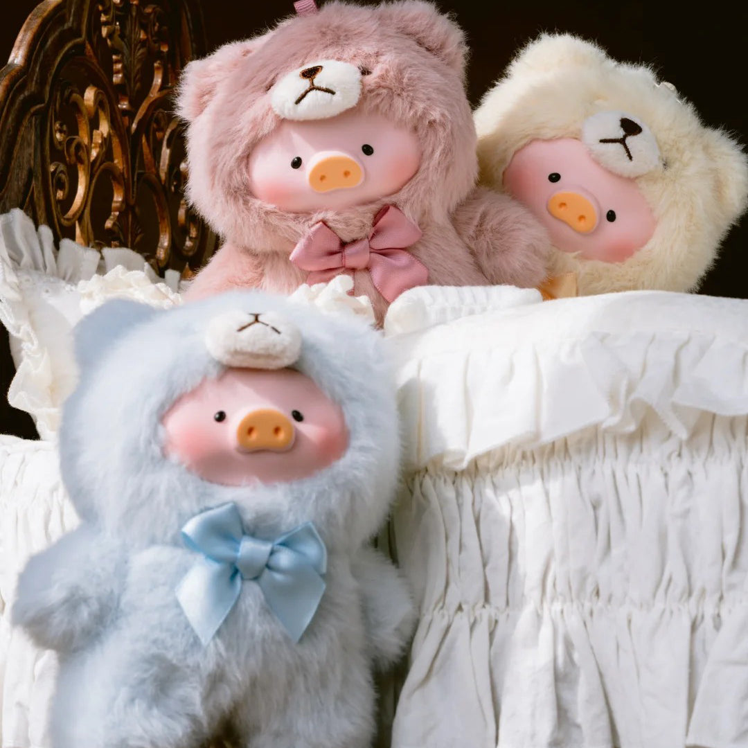 Three plush toys resembling pigs with bear heads, wearing bows, on a decorative background.